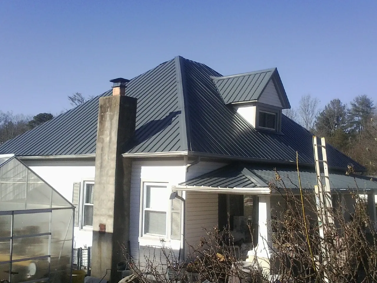 Dark blue standing seam metal roof on a white farmhouse with dormer — Slate & Tile Roof Repair by Roofing Brothers in Elysburg