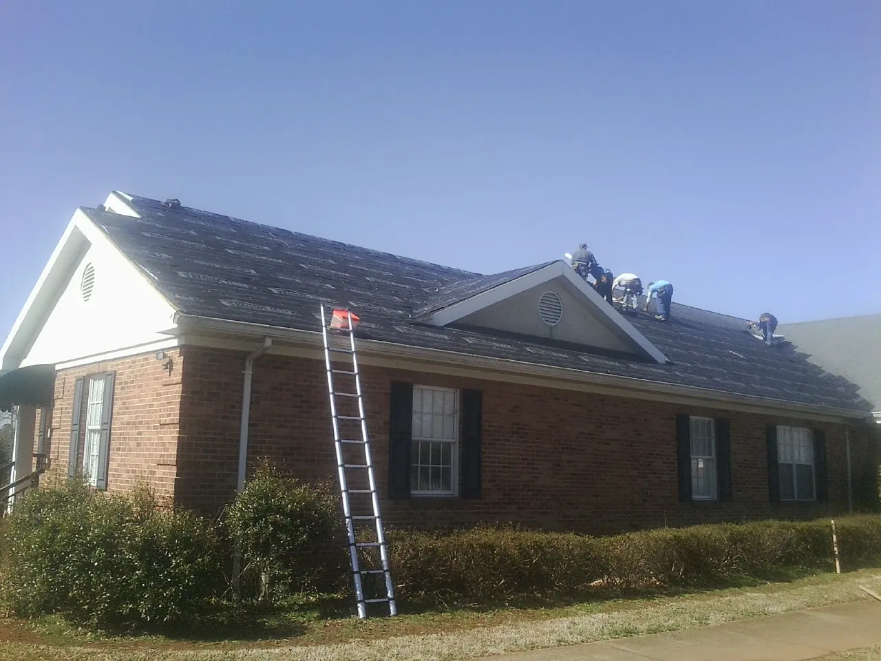 Crew tearing shingles off a brick ranch roof with a ladder set — Emergency Roof Repair work by our crew in Elysburg