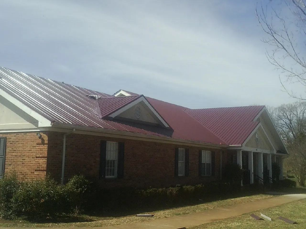 Red metal roof with gabled entries on a long brick building, from a Hail Damage Roof Repair job in Elysburg