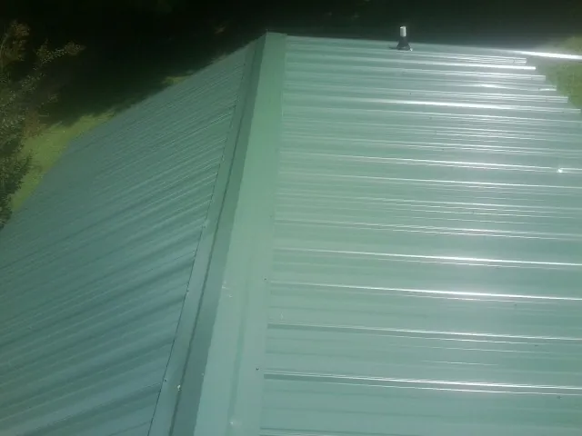 New green metal panels meeting at the ridge of a roof — Flat Roof Repair work by our crew in Elysburg