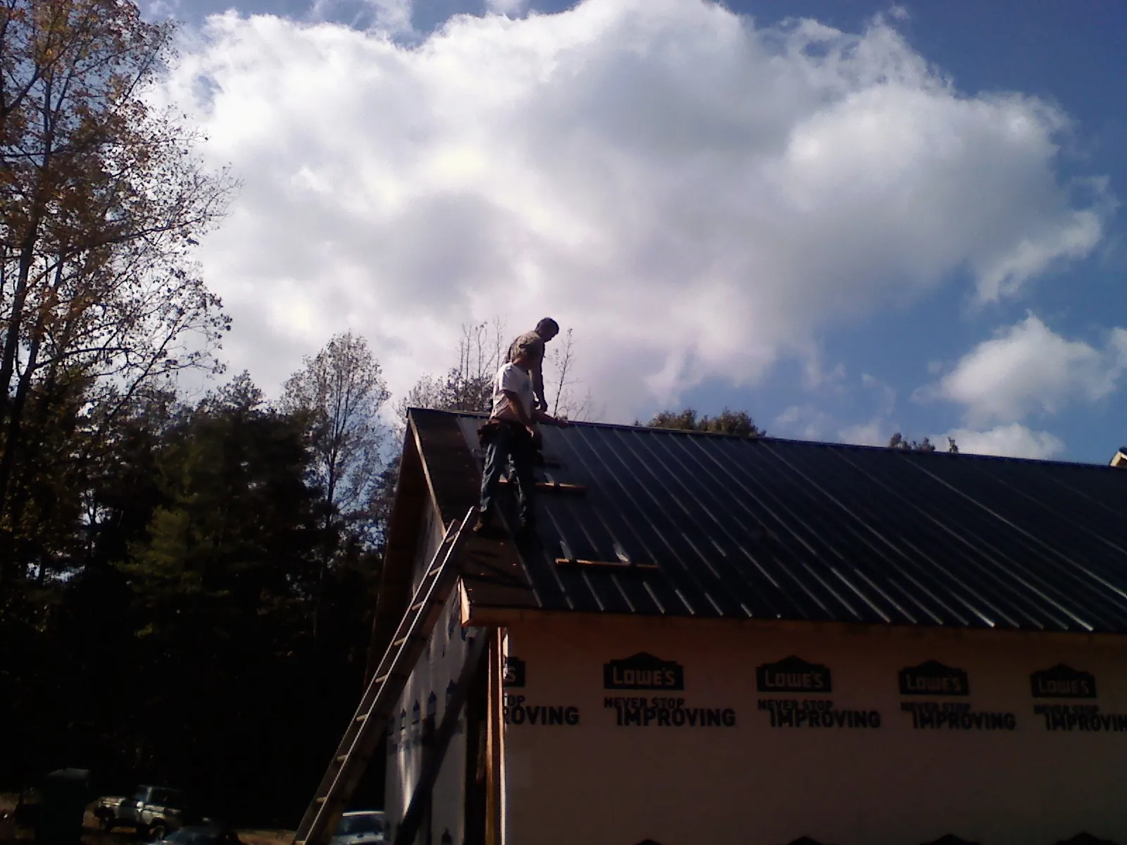 Roofer fastening dark metal panels high against a cloudy sky, from a Roof Inspection job in Elysburg