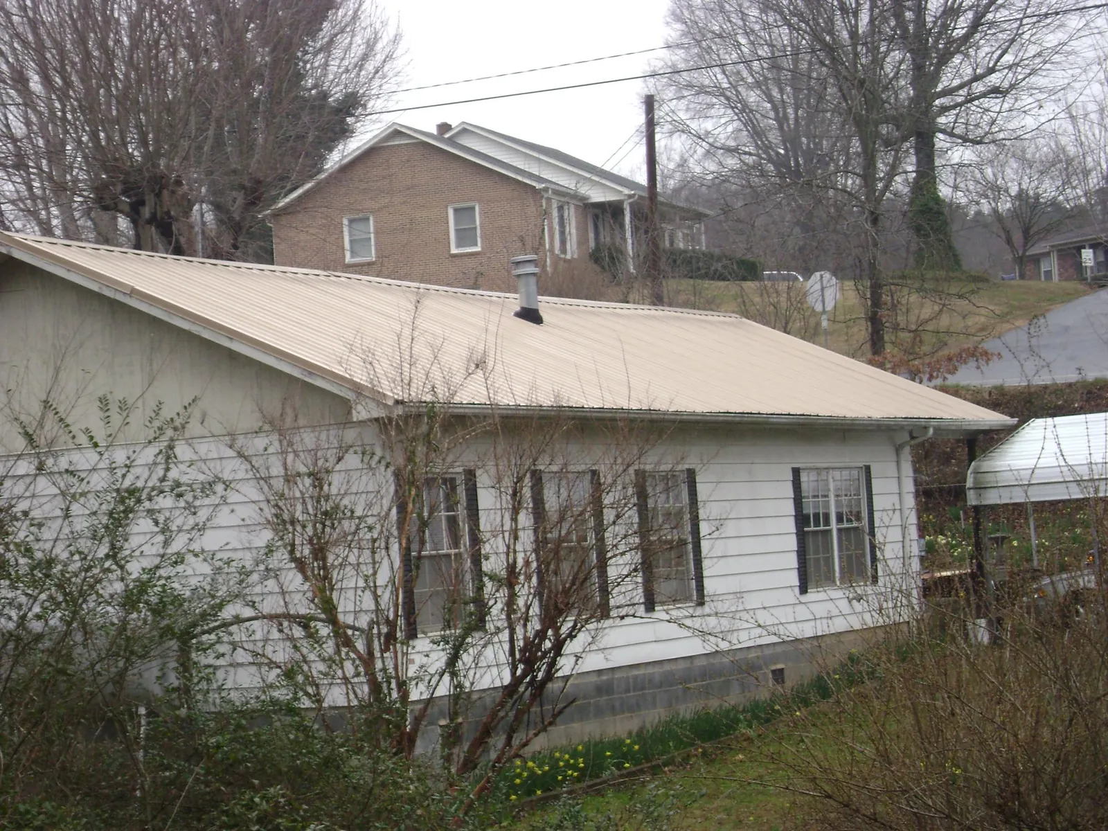 Tan metal roof on a white sided house set into a hillside — Commercial Roofing by Roofing Brothers in Elysburg